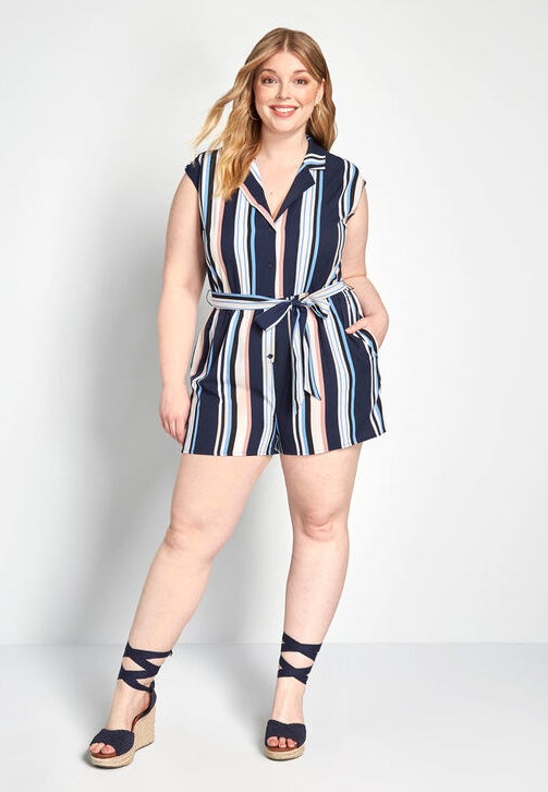 A model wearing the navy, light blue, pink, peach, and white striped, cap-sleeve romper