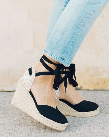 A model wearing a pair of the Soludos lace-up wedges in black