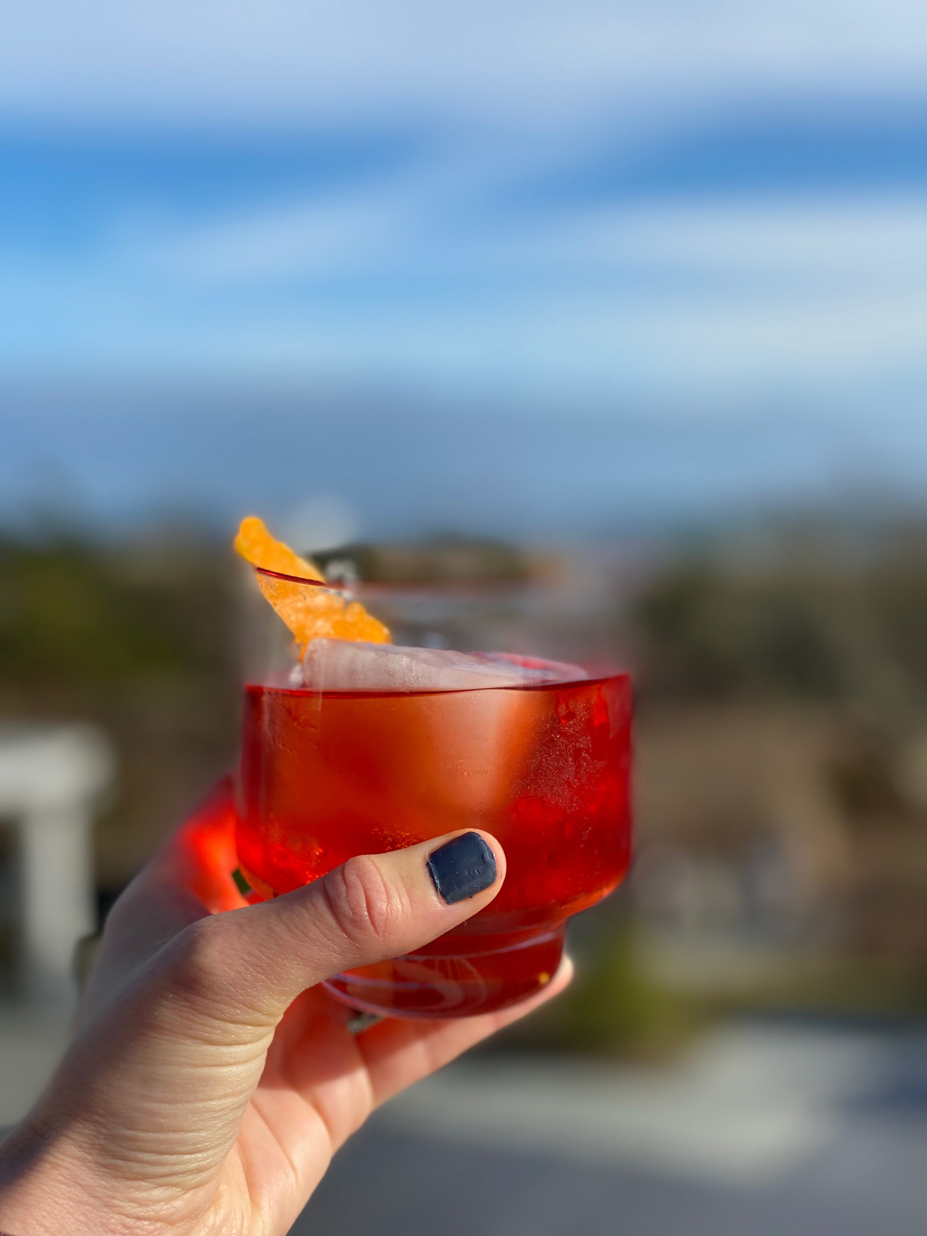 Holding a negroni outside with blue skies in the background.