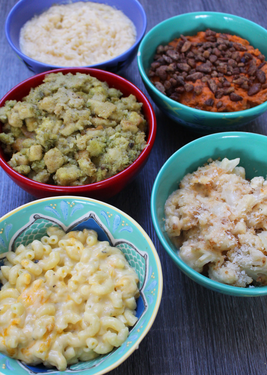 Thanksgiving side dishes like mac &#x27;n&#x27; cheese, scalloped potatoes, stuffing, mashed sweet potato, and regular mashed potatoes in bowls.