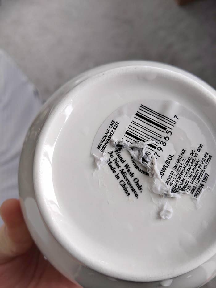 The bottom of a bowl with a sticker that says "microwave safe dishwasher safe" while etching on the bowl reads "hand wash only do not microwave"