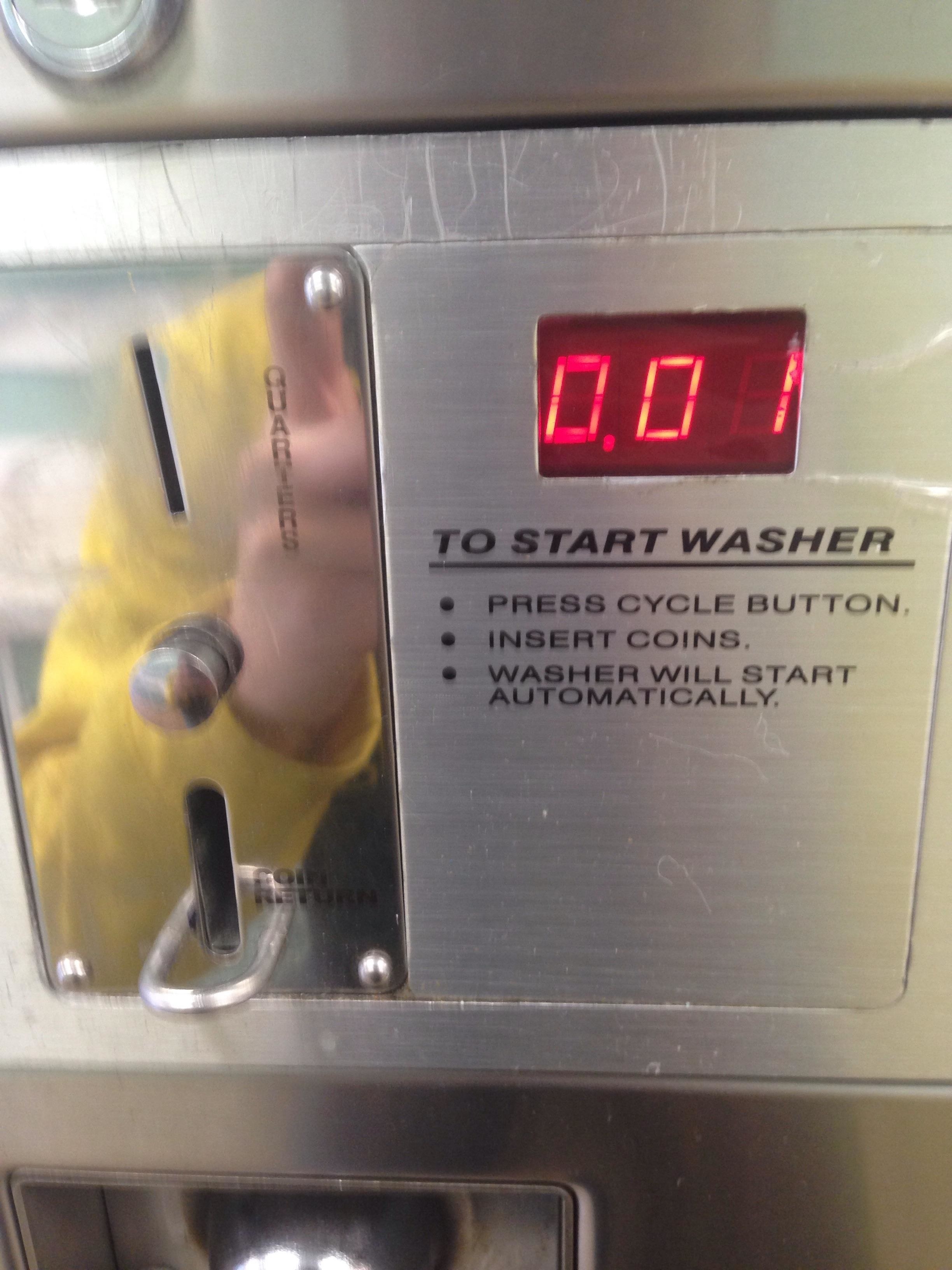 The coin slot on a washing machine that takes quarters with a digital display that reads 0.01