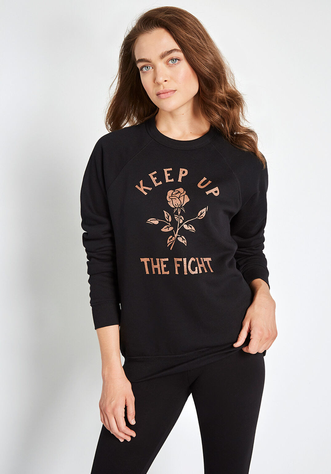 a model wearing the black sweatshirt with a rose gold colored rose and stem on it and the words &quot;keep up the flight&quot;