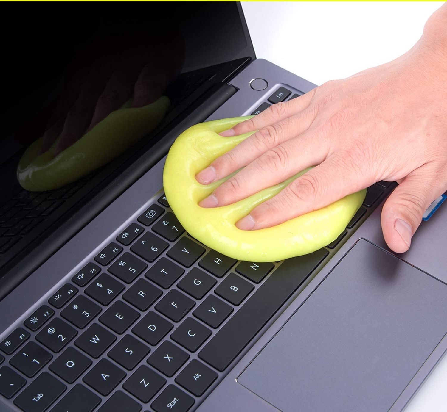 Yellow cleaning gel that looks similar to slime on a keyboard with a model&#x27;s hand on it