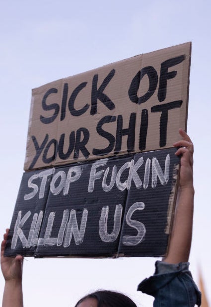 A protest sign reads &quot;Sick of your shit, stop fucking killin us&quot;.