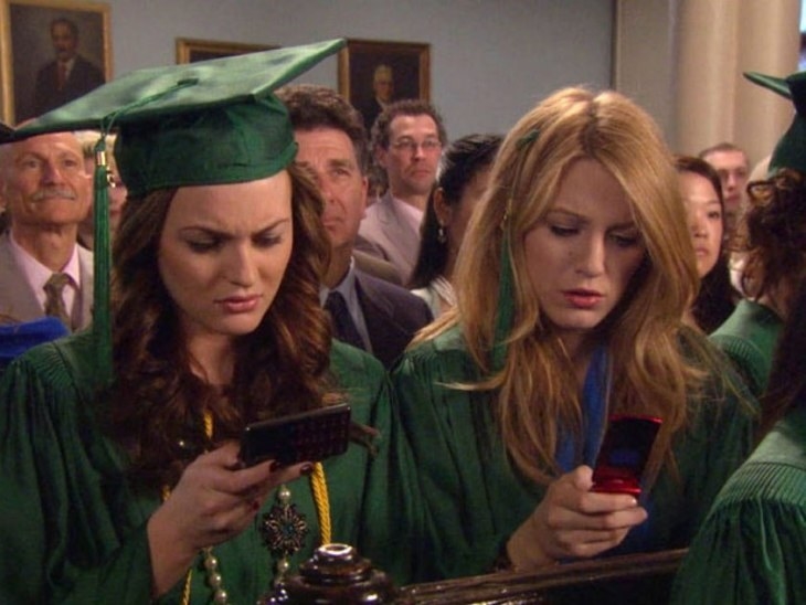 Serena and Blair looking at their phones at graduation