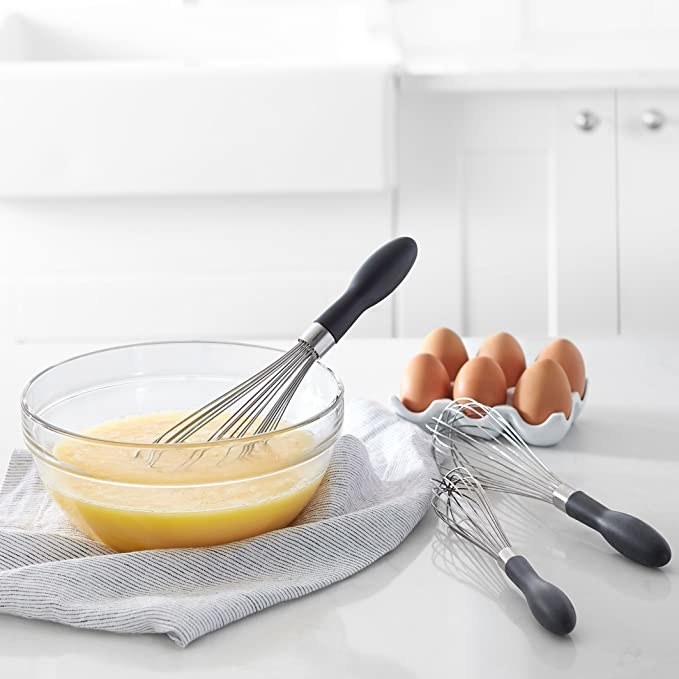 The whisks pictured with some eggs and a bowl of whisked eggs.