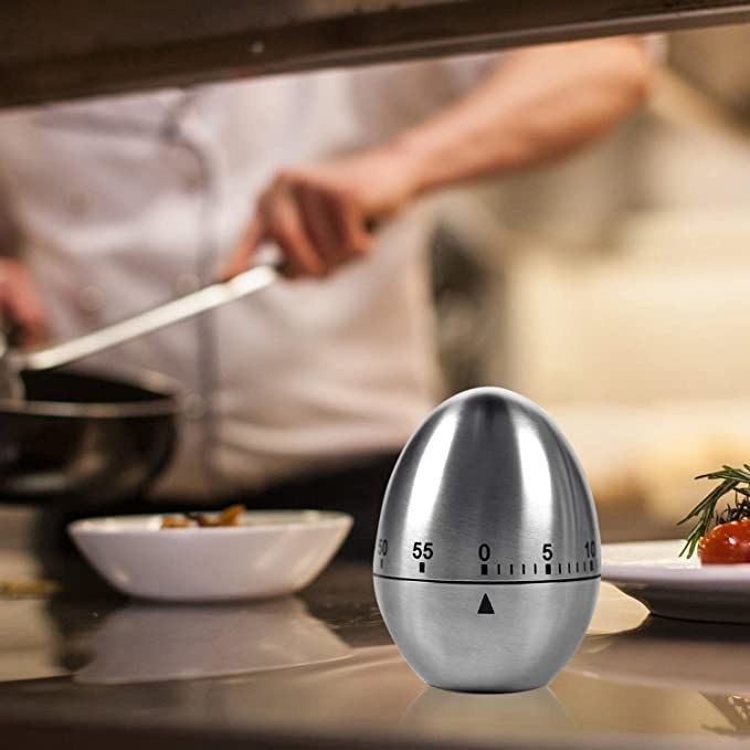 Egg timer on the kitchen table with a person cooking in the background