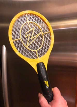 reviewer's hand holding up the zapper that looks like a small tennis racket