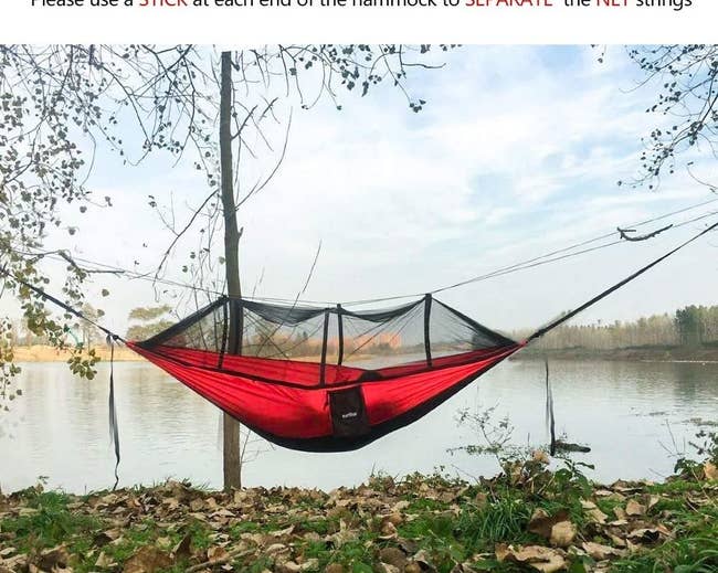 red hammock strung up between two trees with a mosquito net on top