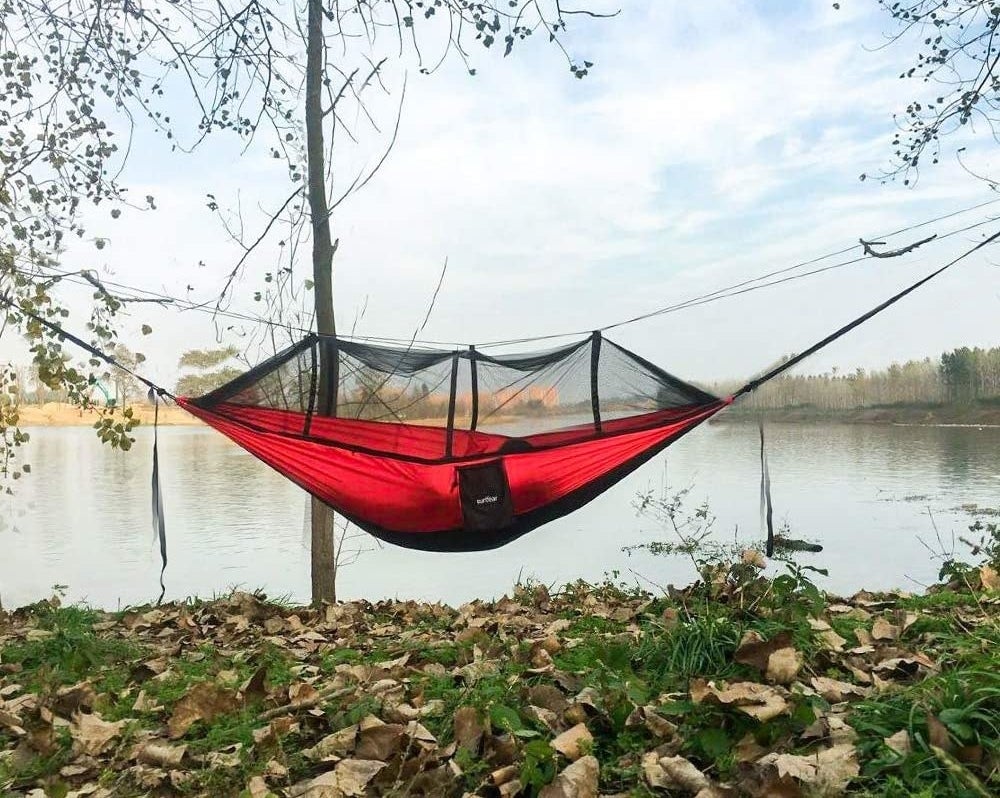 red hammock strung up between two trees with a mosquito net on top