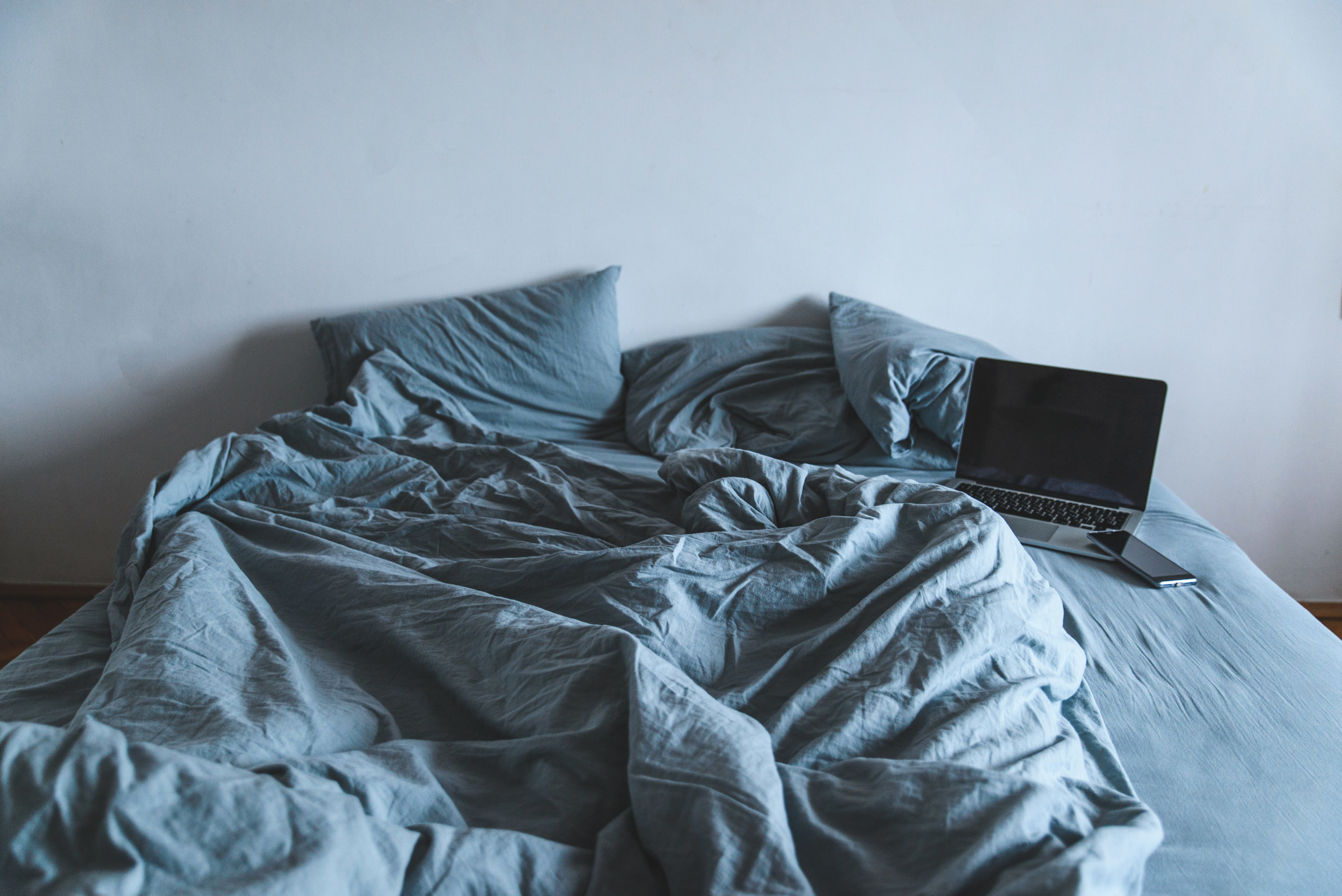 A cozy-looking but unmade bed with a laptop