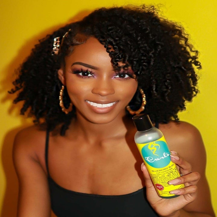 Model holding the bottle of product and showing her ringlet curls 