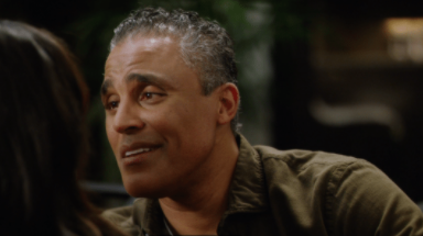Rick Fox leans forward as if to kiss his scene partner, or whisper something in their ear