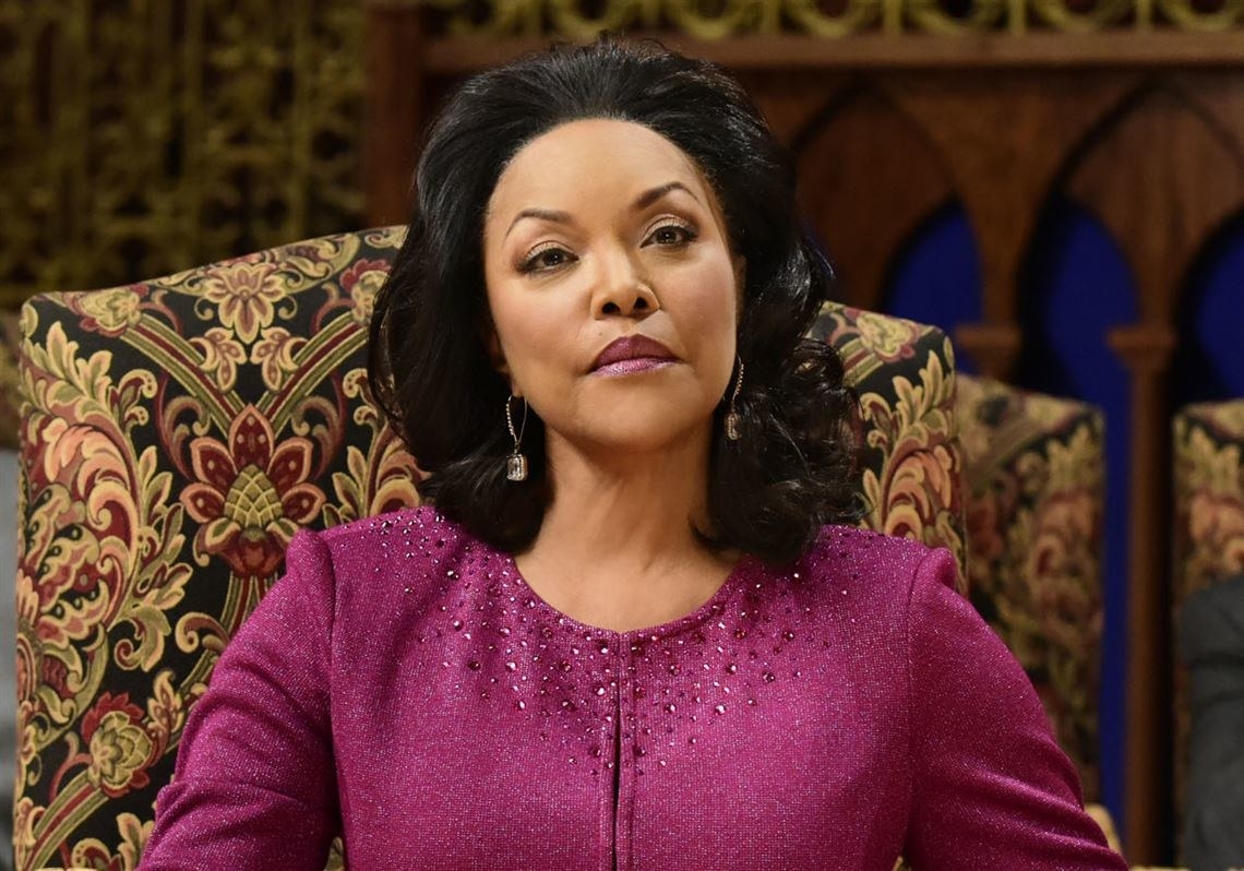 Lynn Whitfield sits on the pulpit in a chair, with her face slightly tense