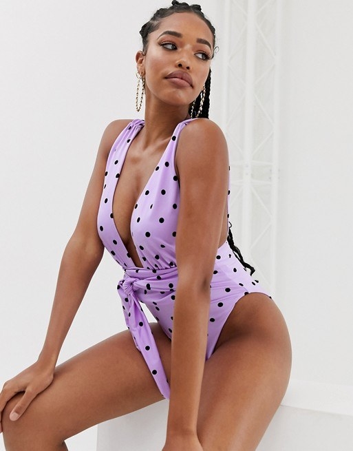 model wears lavender swimsuit with waist sash and black polka dots 