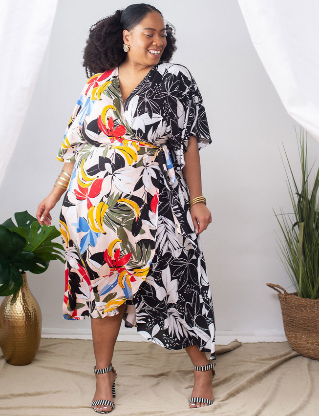 model wears a wrap dress that is half colorful tropical print with bananas and the other half is black and white flowers 