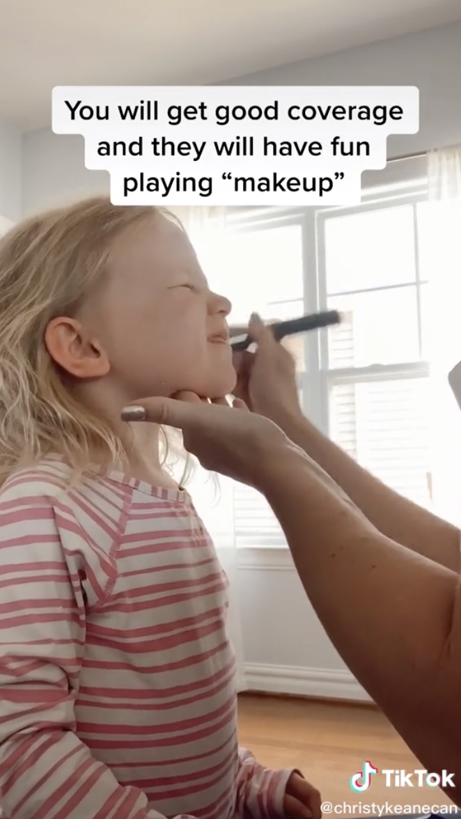Christy putting sunscreen on her daughter with a makeup brush.