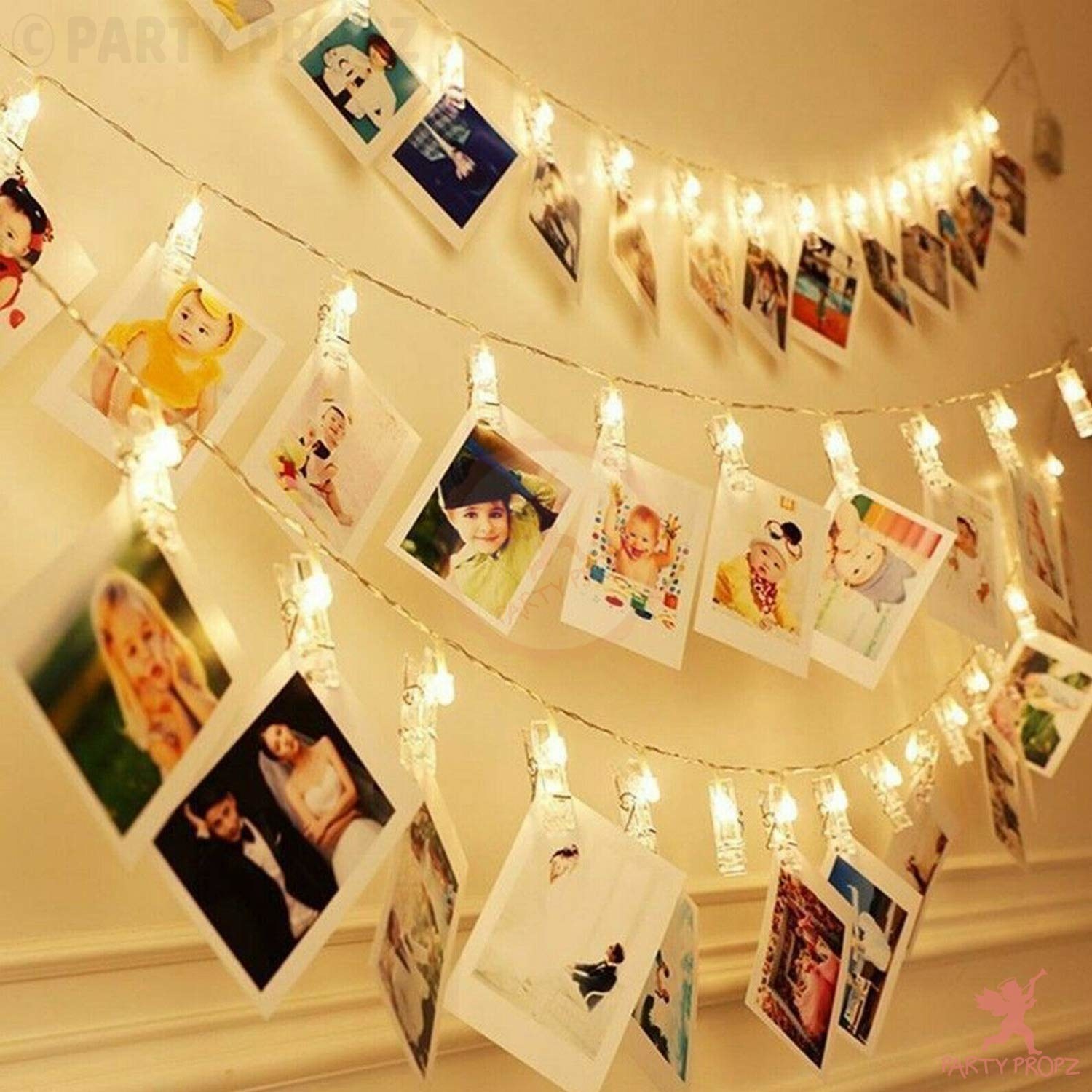 A string of fairy lights hanging against a wall, with multiple photos attached to its clips