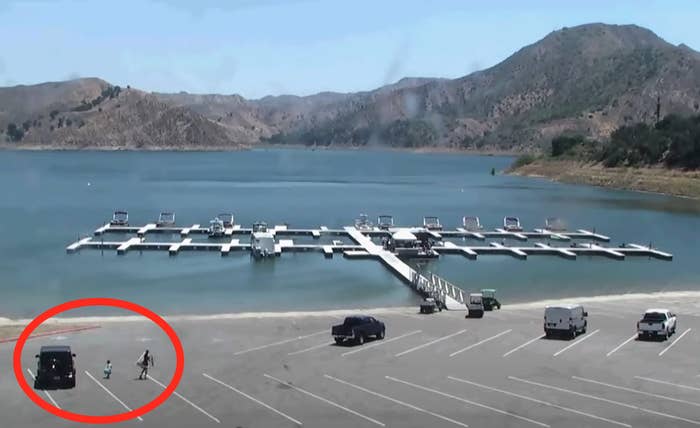 The photo shows two people walking from a car in the parking lot of a marina.