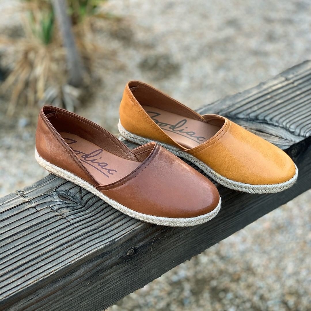 Two espadrille flats in dark brown and mustard with a braided outsole sitting on a piece of wood