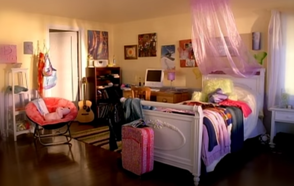A sunny teen/tween girls bedroom with a desk and a white sleigh-bed with a pink mosquito net on top. 