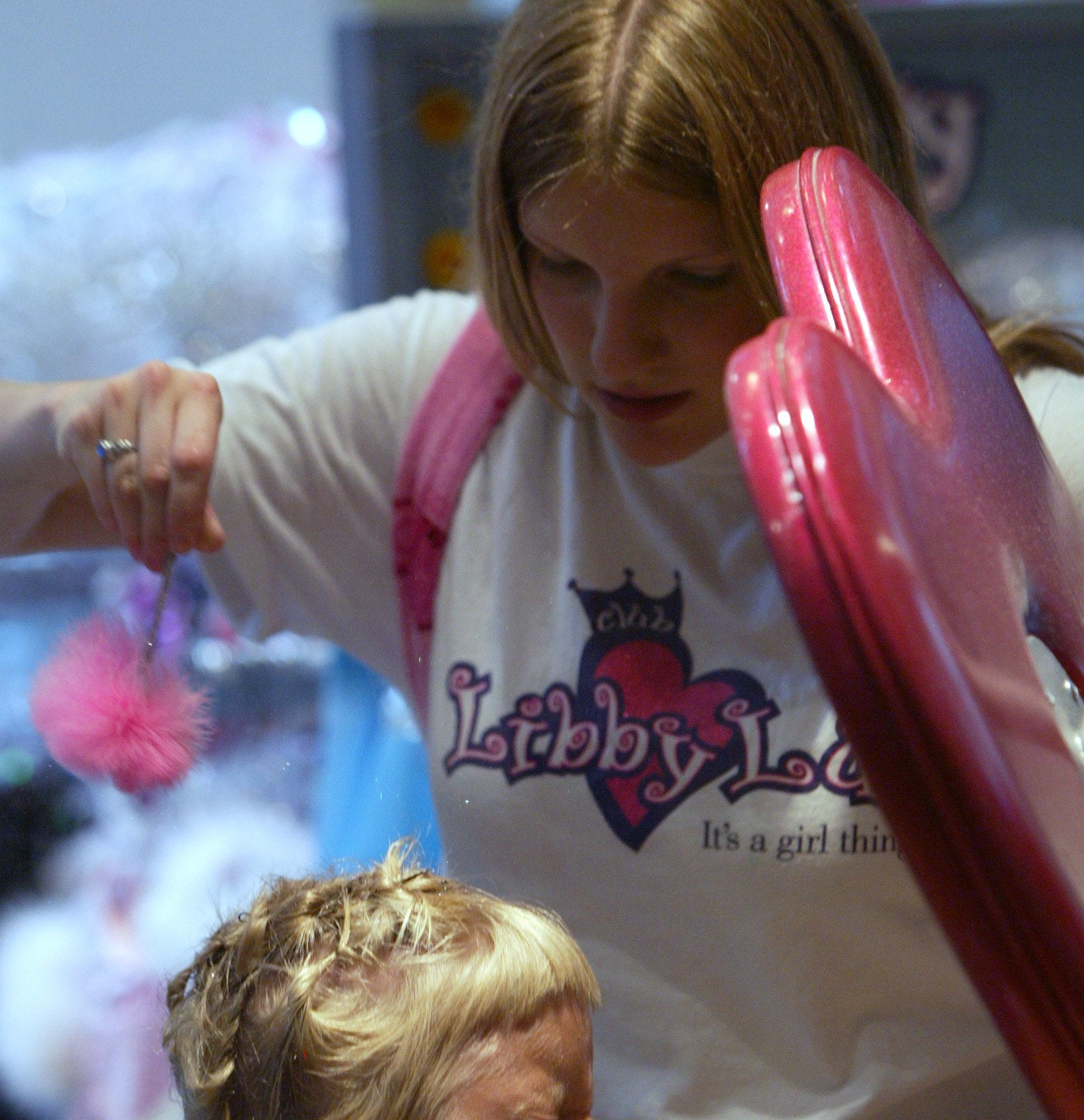 Libby Lu employee sprinkling glitter into a little girls hair.