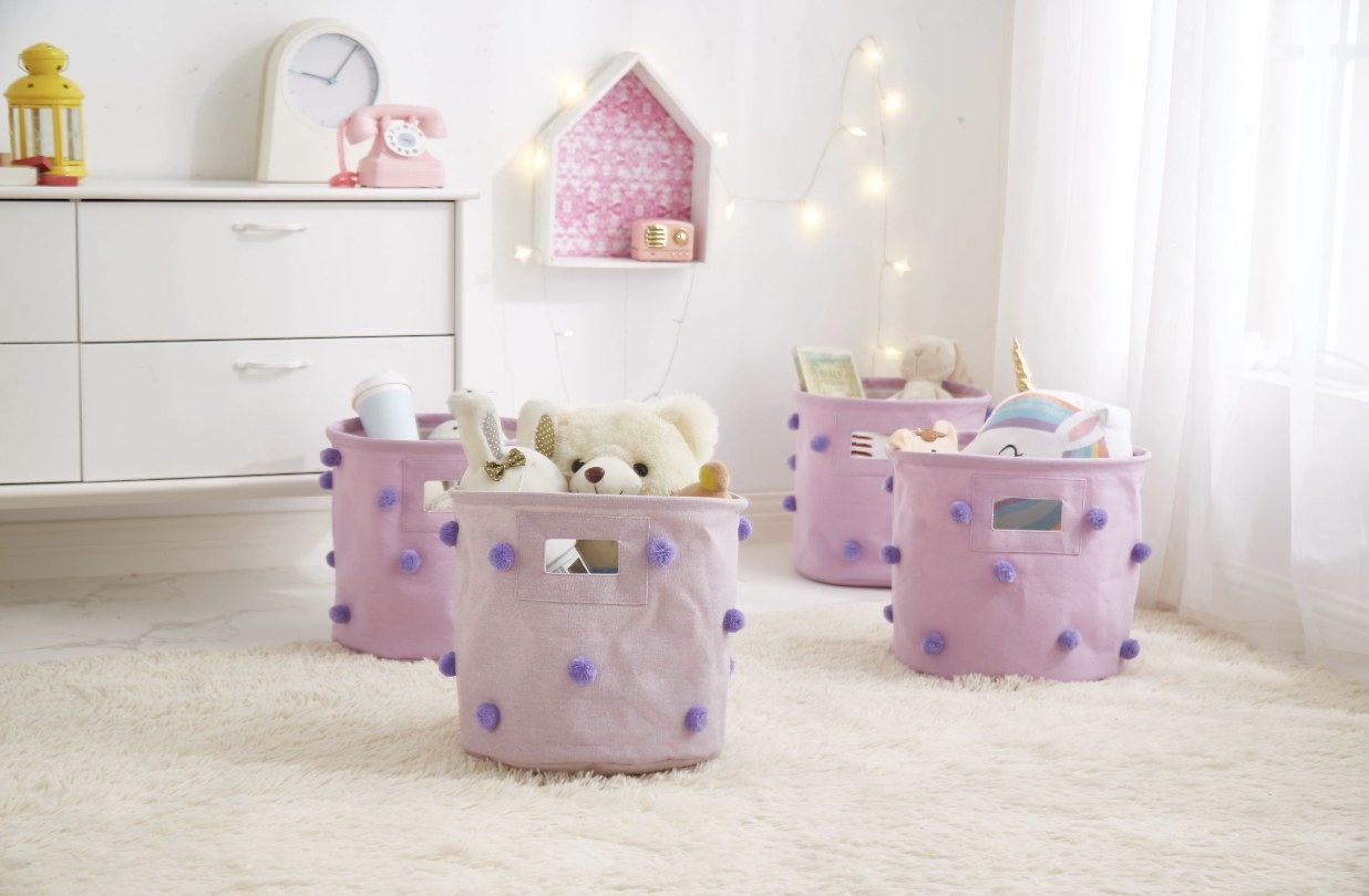 four purple buckets with darker purple pom poms on them storying stuffed animals