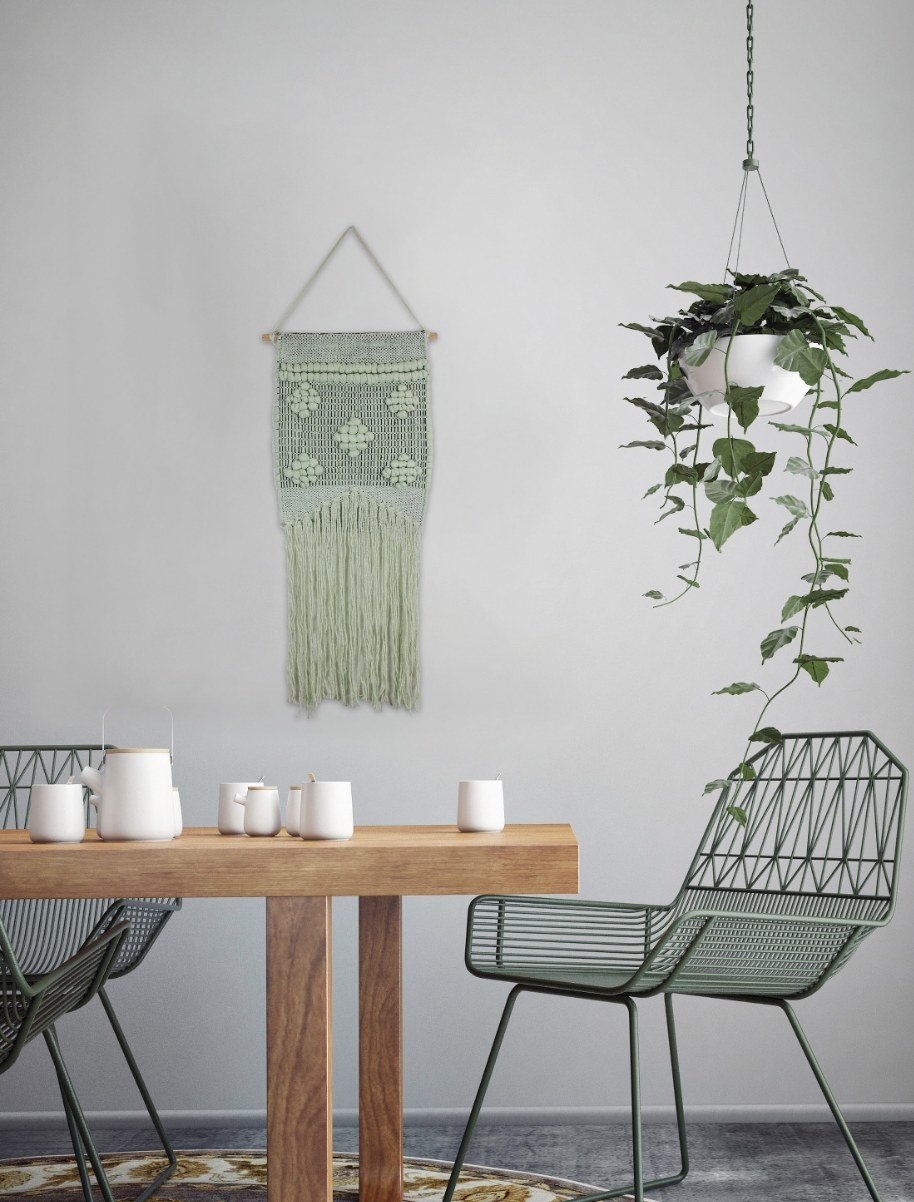 a light green macrame wall hanger with long fringe and a woven design