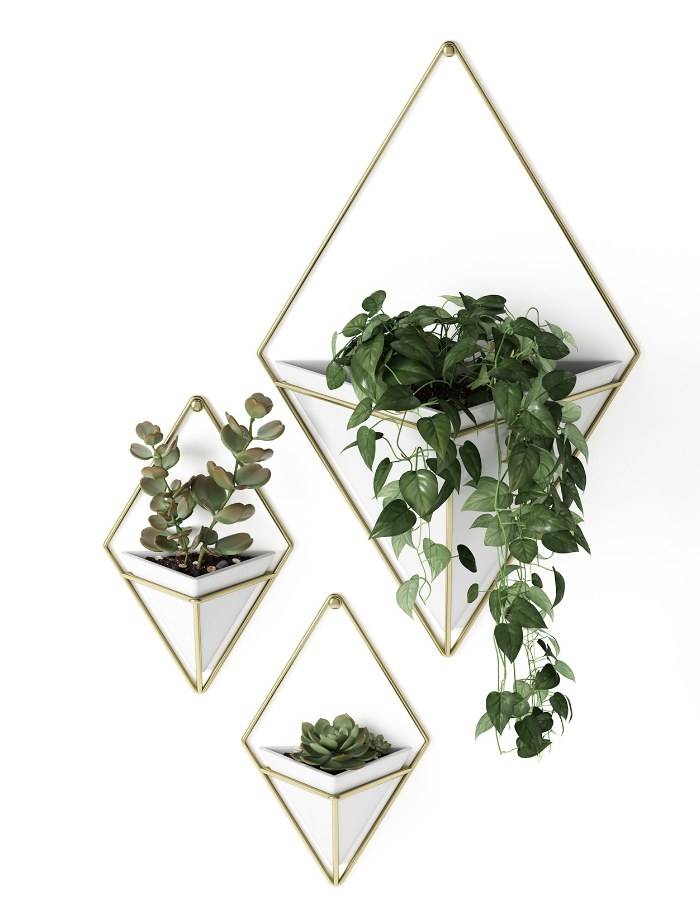 a set of three triangle white hanging vases with gold cages around them, two small and one large