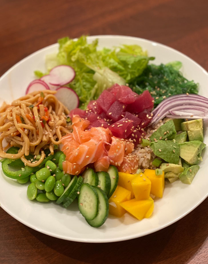 A poke bowl with diced tuna, salmon, sesame noodles, and lots of chopped vegetables over rice and lettuce.