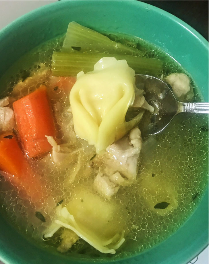 A bowl of chicken broth with tortellini, carrots, celery, and chicken.