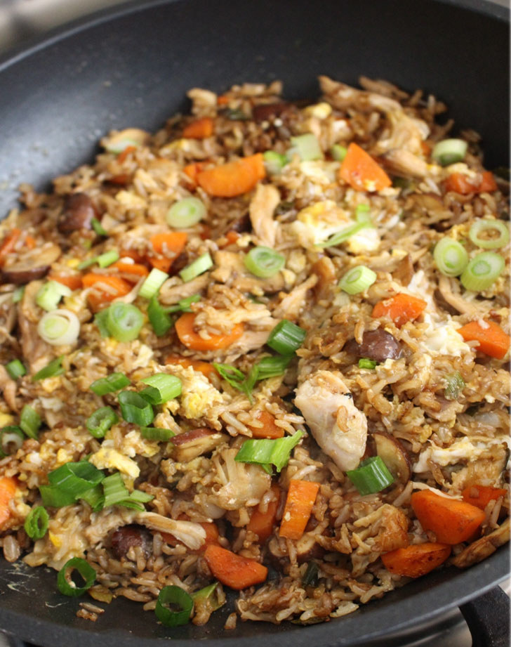 A skillet full of fried rice with chicken, vegetables, and scallions.