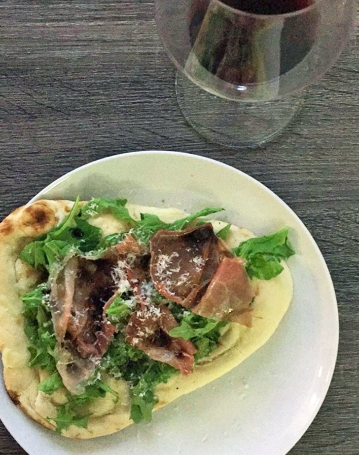 A piece of naan topped with prosciutto, arugula, and parmesan cheese.