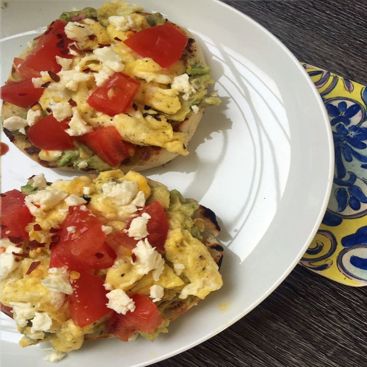Scrambled eggs with feta cheese and tomatoes on top of English muffins with mashed avocado.