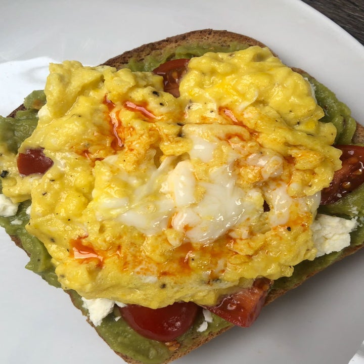 A slice of toast topped with mashed avocado, feta, scrambled eggs, and chili oil.
