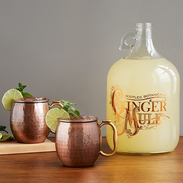 Two Moscow Mule copper mugs next to a bottle of ginger beer