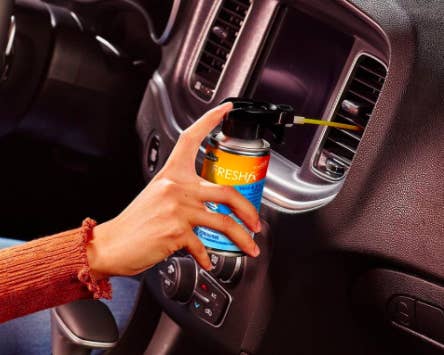 Hand sprays can of Armor All Car Air Freshener and Cleaner to clean vents inside a black vehicle