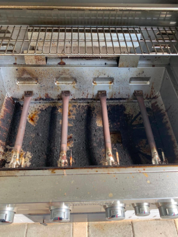 A grill covered in burned-on stains and grease before using a grill cleaner