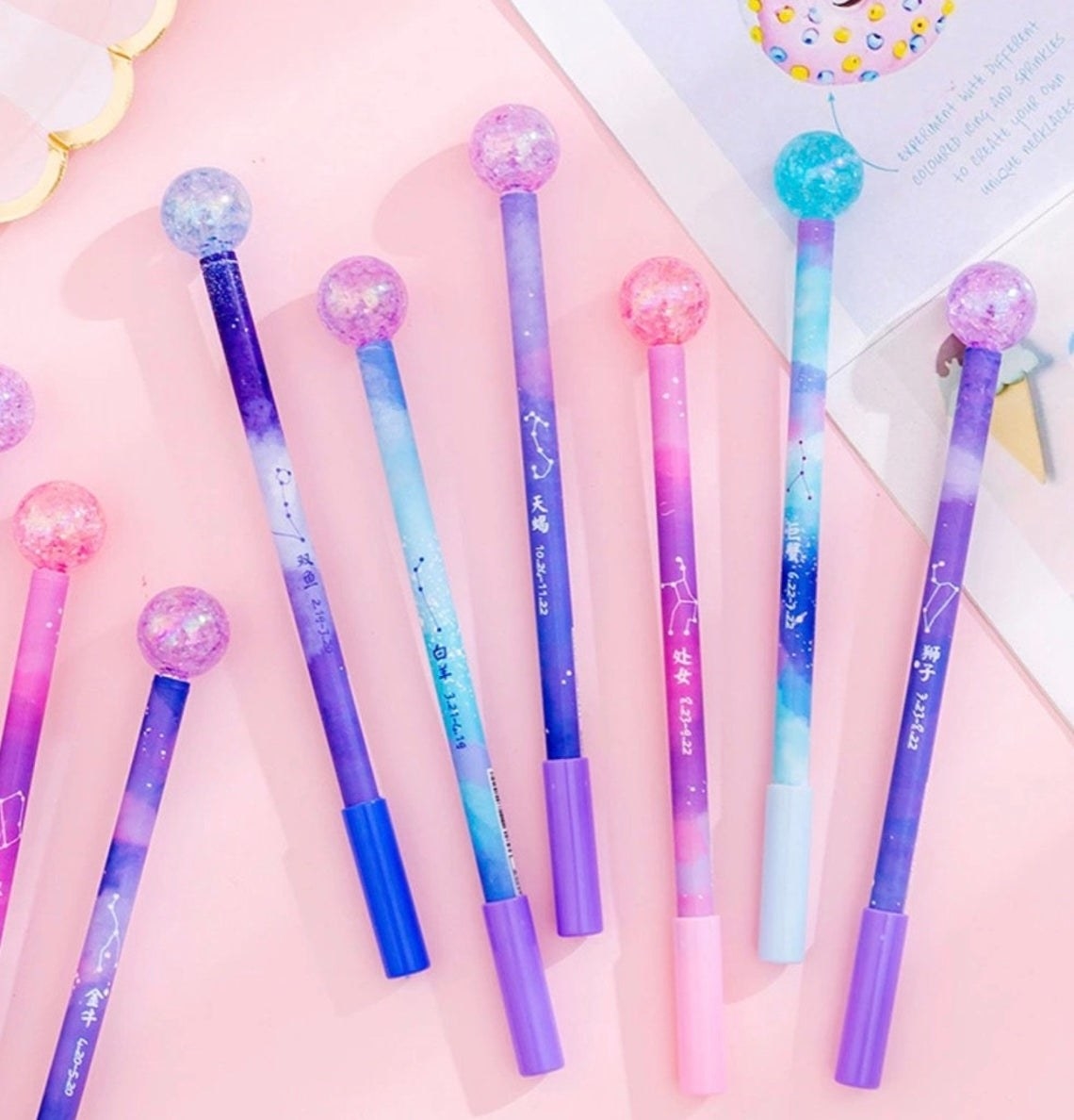 The pens, which have glittery balls on the top and are printed with galaxy and constellation patterns, in various colors. They all have caps