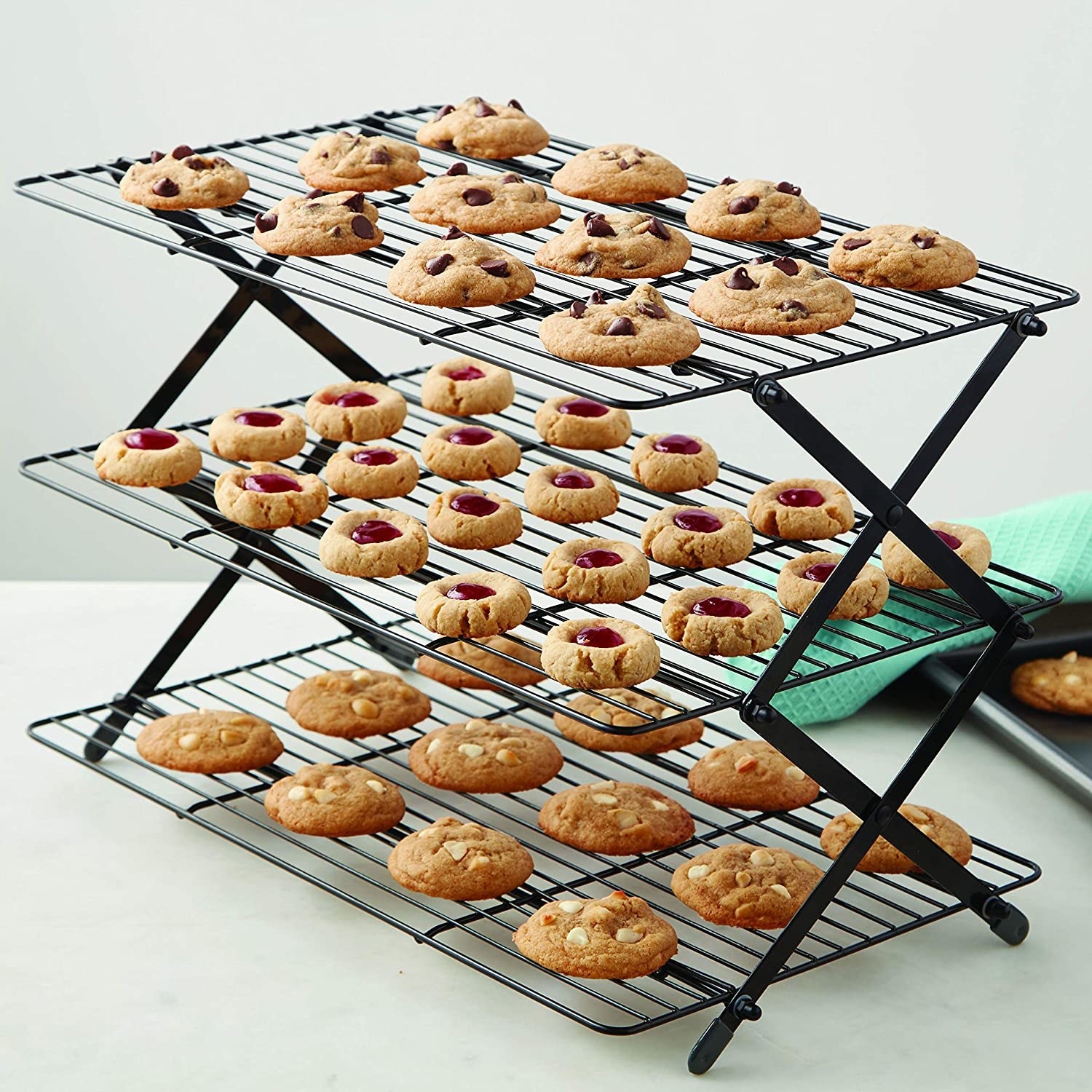 A three tier cookie rack stands on a counter top full of different cookies