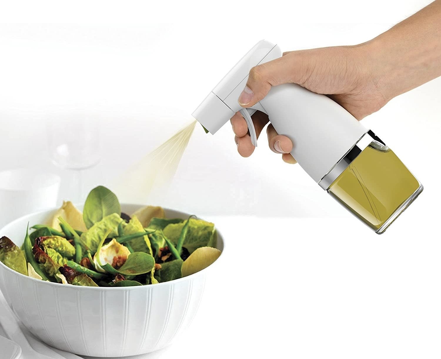 A person uses the mister to spritz a salad with olive oil