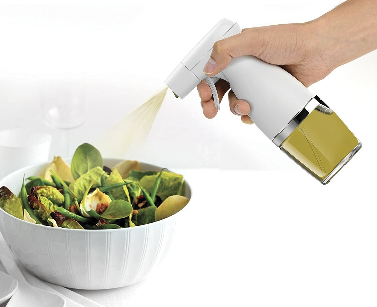 A person uses the mister to spritz a salad with olive oil