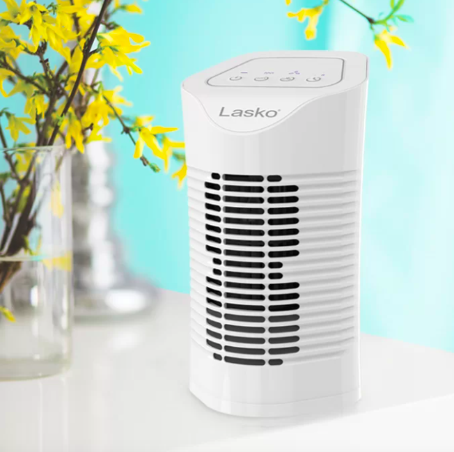 A white desktop air purifier next to a clear vase with yellow flowers