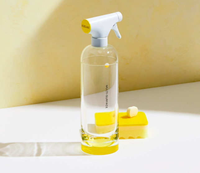 Clear Blueland reusable cleaning bottle and yellow Fresh Lemon tablet on a white countertop