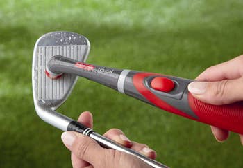 Hand holds red mini power scrubber while cleaning the front part of a golf club