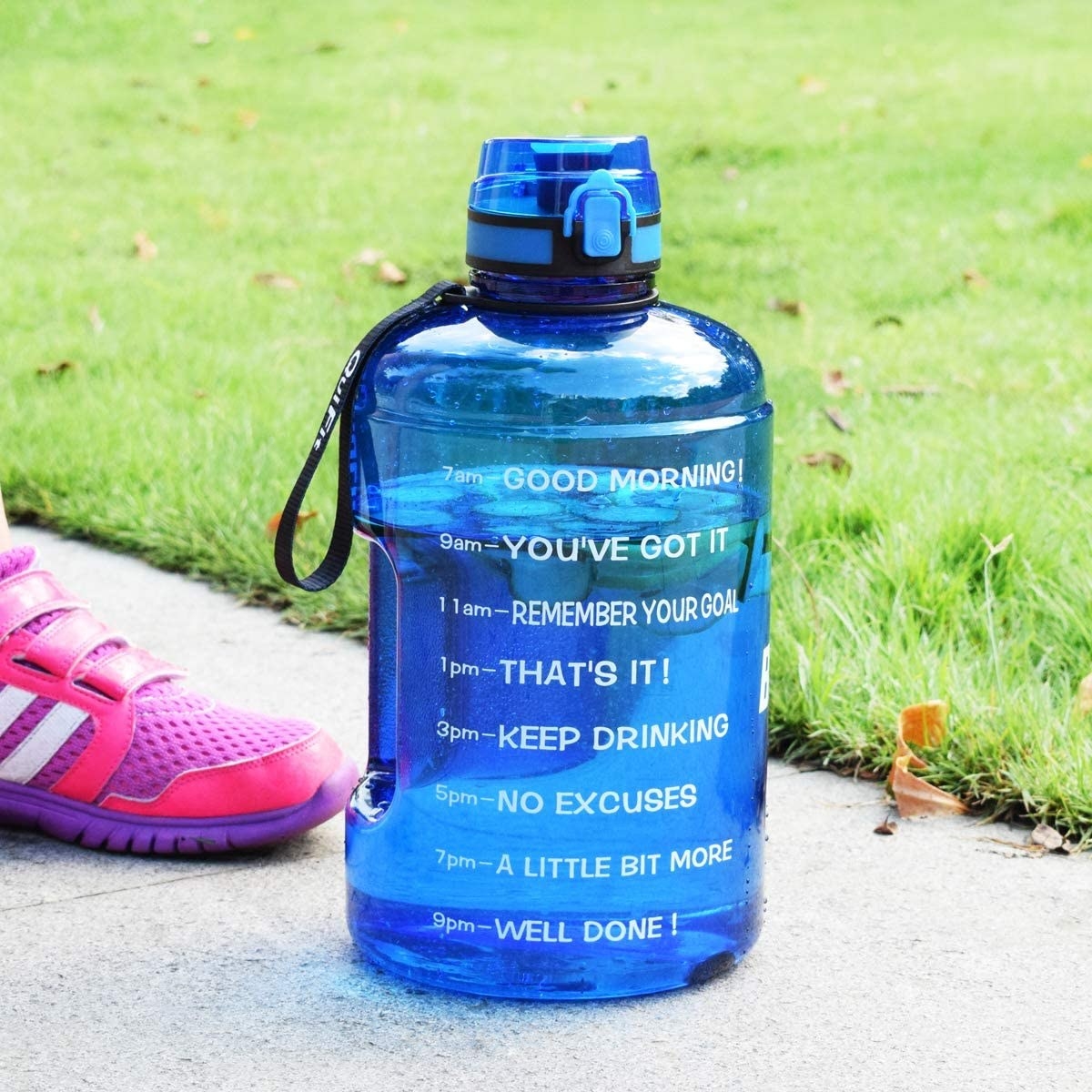 A time-marked waterbottle on the pavement beside a lawn and someone's foot