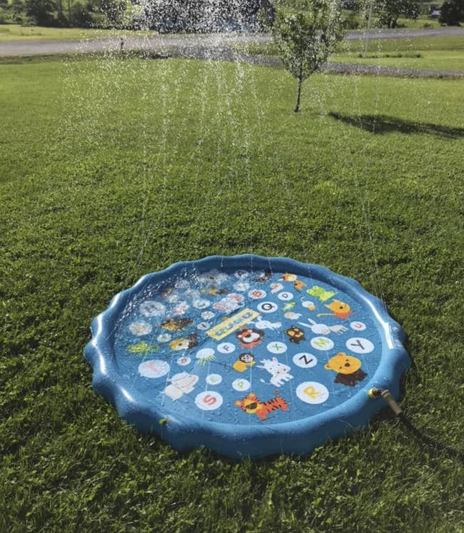 A reviewer's small inflatable pool with water shooting up from the squirters all around the rim of it. It's sitting in a yard, attached to a hose.