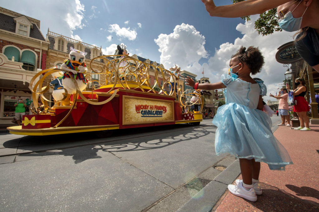 A little girl in a Cinderella dress and a mask waves to Daisy Duck during the cavalcade