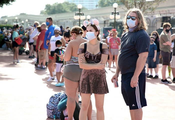 A crowd of people wearing  masks waits to enter the park